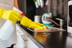 someone with gloves, cleaning spray, and a sponge cleaning a countertop 